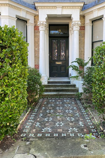 A detailed view of a well-maintained front garden featuring a neatly trimmed lawn with lush green grass, bordered by a variety of flowering plants and shrubs. The garden beds are edged with dark mulch